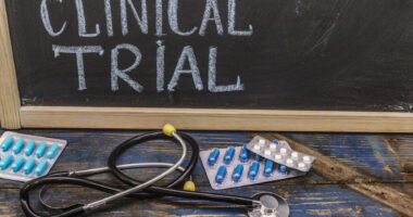 A stethoscope and oral medication packets are seen in front of a blackboard with the words 