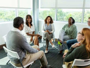A group of adults sit in a circle during a therapy session.