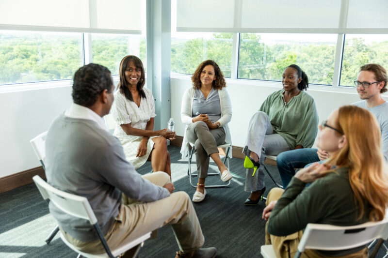 A group of adults sit in a circle during a therapy session.