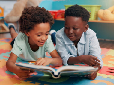 Two children lying on a mat read a book together.