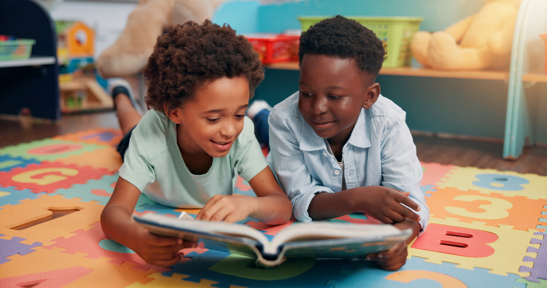 Two children lying on a mat read a book together.