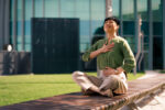 A woman is sitting on a bench practicing breathing exercises with her eyes closed and hands on her chest and stomach.
