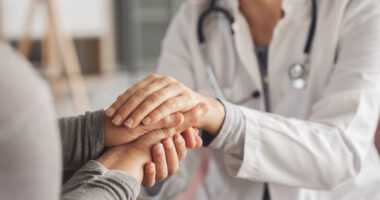 A person in a lab coat holds hands with a patient.