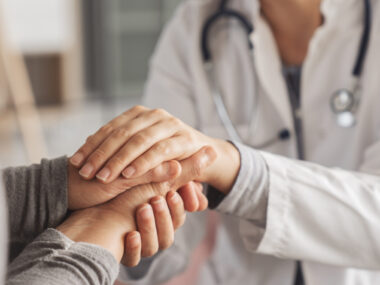 A person in a lab coat holds hands with a patient.