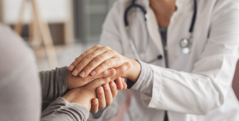 A person in a lab coat holds hands with a patient.