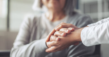 Two hands embrace the hand of a woman whose face is partially obscured.