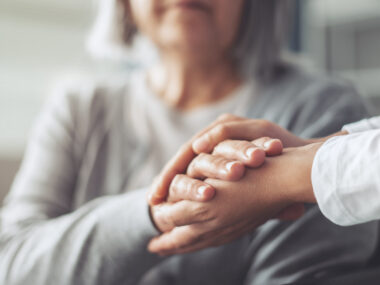 Two hands embrace the hand of a woman whose face is partially obscured.