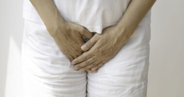 A person is shown standing, with hands placed over the groin area.