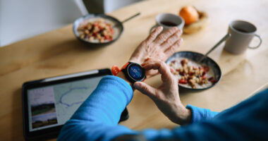 A woman adjusts a smartwatch while eating a light breakfast.