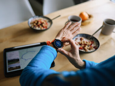 A woman adjusts a smartwatch while eating a light breakfast.