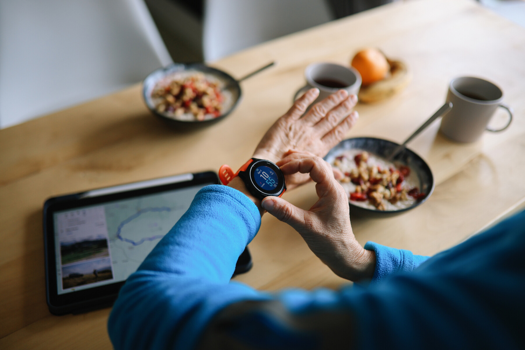 A woman adjusts a smartwatch while eating a light breakfast.