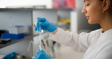 A person in a white coat works in a lab.