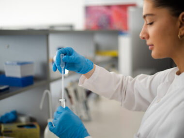 A person in a white coat works in a lab.