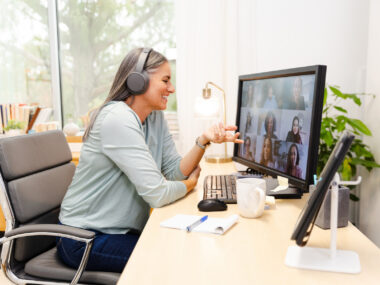 A photo of an adult woman using a computer in a home office, on a video conference with colleagues.