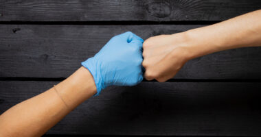 A hand in a blue medical glove and a hand without a glove bump fists.