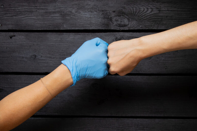 A hand in a blue medical glove and a hand without a glove bump fists.