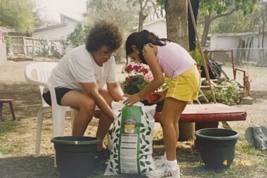 A young child helps a woman who is seated open a bag of soil