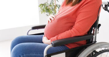 A pregnant woman sits in a wheelchair.