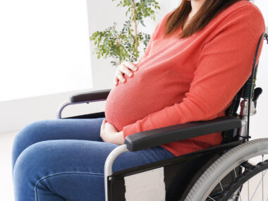 A pregnant woman sits in a wheelchair.