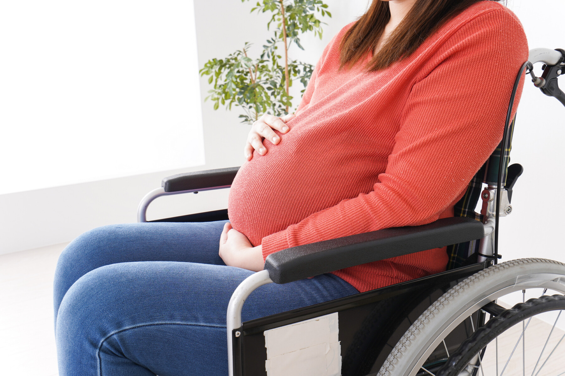 A pregnant woman sits in a wheelchair.