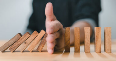 A man stops the domino effect by using his hand to prevent a line of wooden blocks from continuing to fall.