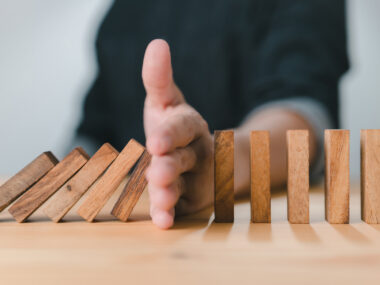 A man stops the domino effect by using his hand to prevent a line of wooden blocks from continuing to fall.