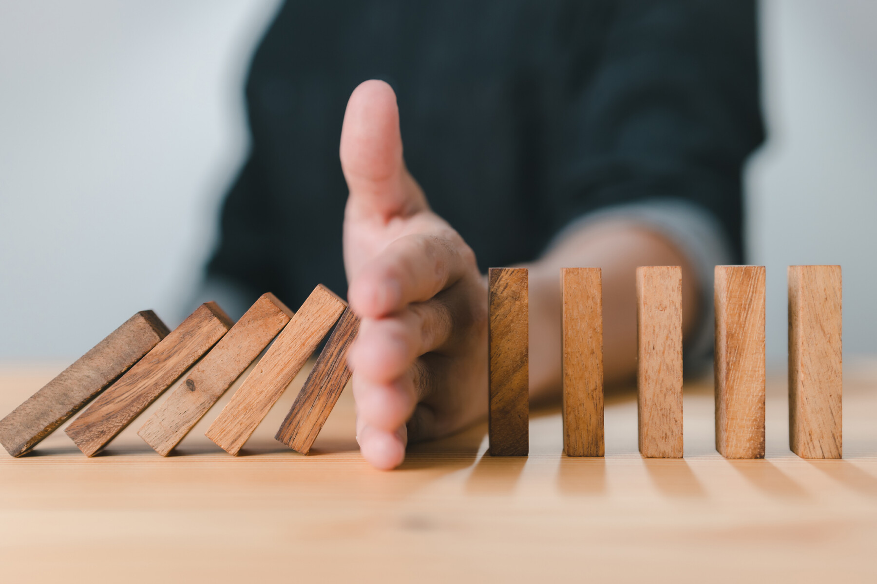 A man stops the domino effect by using his hand to prevent a line of wooden blocks from continuing to fall.