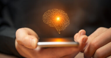 An AI image of the human brain is seen above a smartphone held in a person's hand.