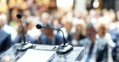 A microphone and some papers sit on a podium in front of a crowd.