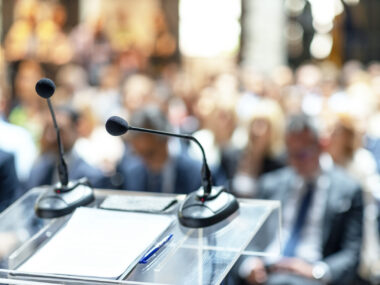 A microphone and some papers sit on a podium in front of a crowd.