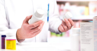 A person in white lab coat holds pill bottles in both hands.