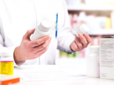 A person in white lab coat holds pill bottles in both hands.