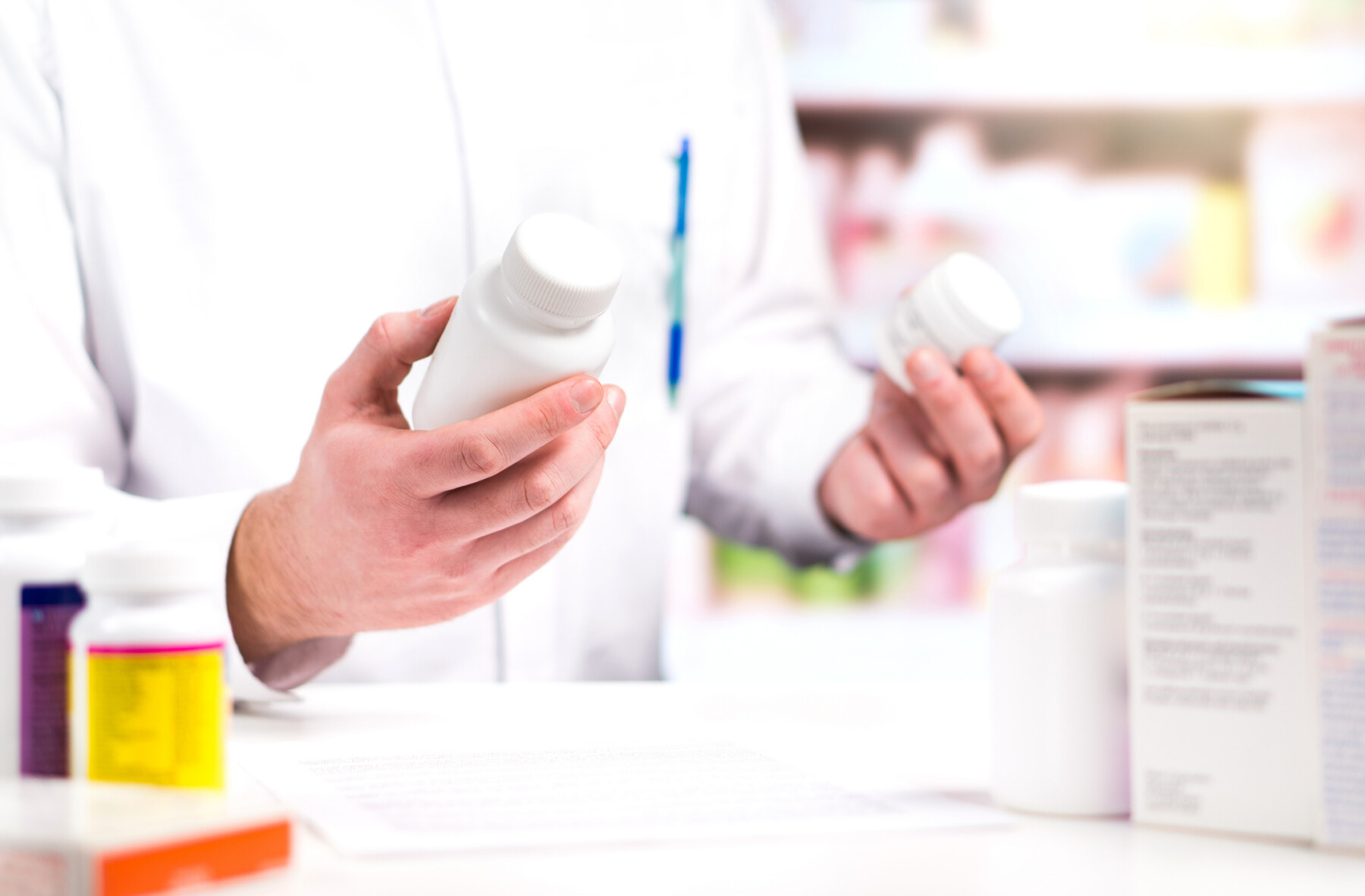 A person in white lab coat holds pill bottles in both hands.