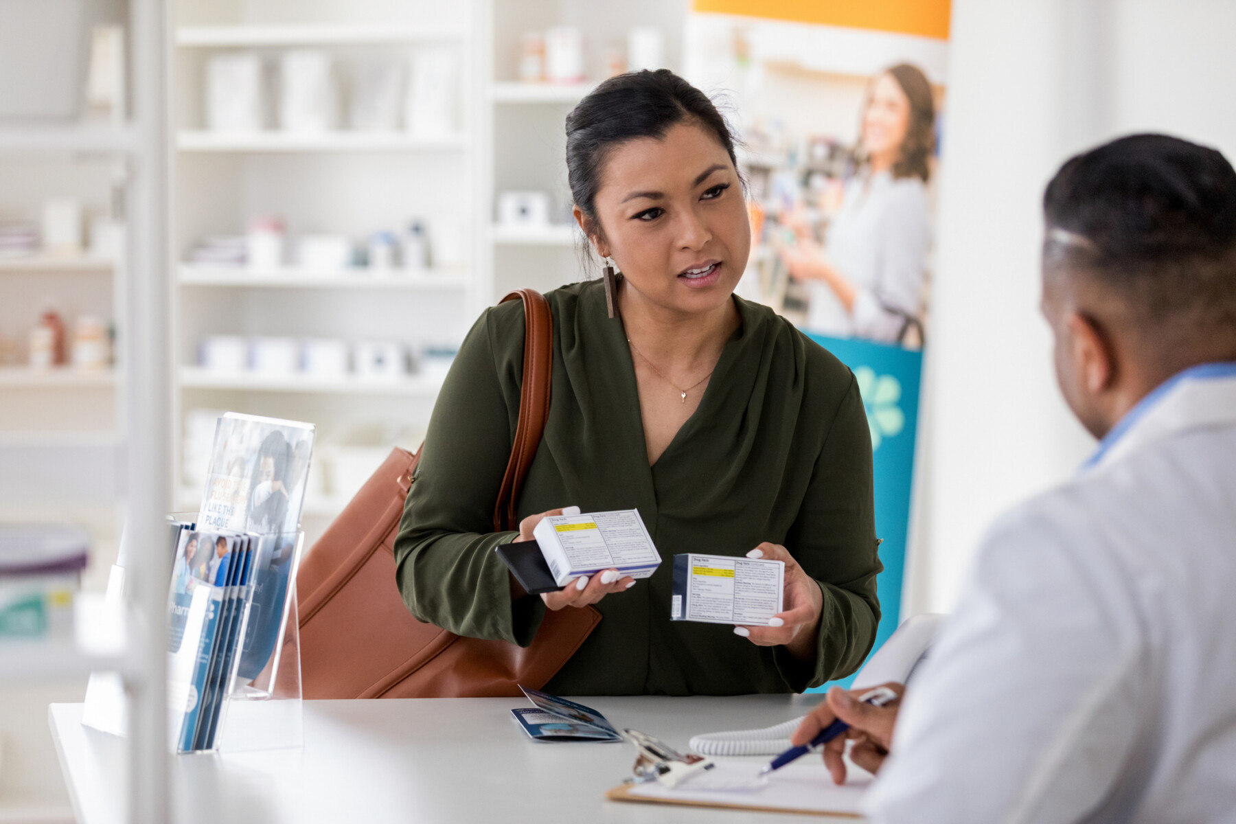A drugstore customer, seen holding two medication boxes, consults with a pharmacist.