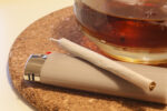 A photo shows a marijuana cigarette and a glass of amber liquid.