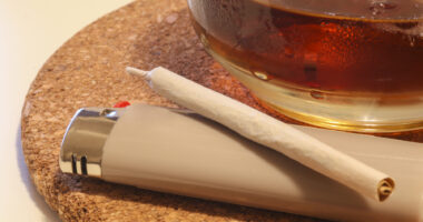 A photo shows a marijuana cigarette and a glass of amber liquid.