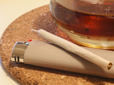 A photo shows a marijuana cigarette and a glass of amber liquid.