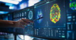 A doctor points at a patient's scan on a desktop computer monitor.