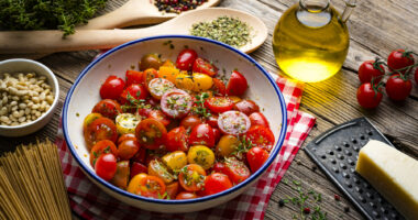 A bowl of vegetables are pictured next to a bottle of olive oil on a wooden table.