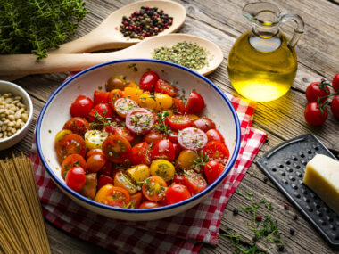A bowl of vegetables are pictured next to a bottle of olive oil on a wooden table.