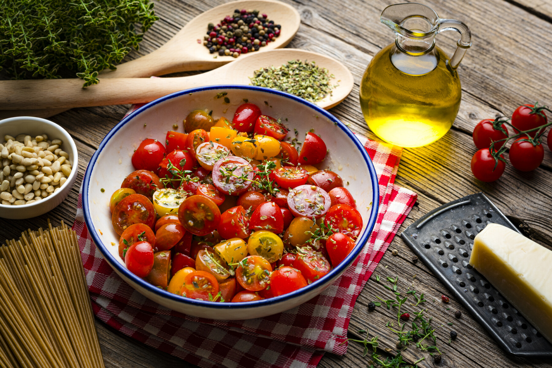 A bowl of vegetables are pictured next to a bottle of olive oil on a wooden table.