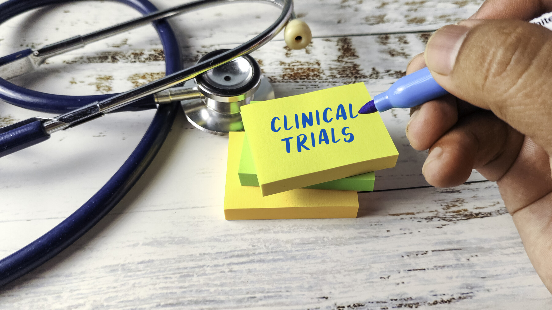 A hand holding a blue marker is seen next to a stethoscope and a stack of small Sticky Note pads, with the words 