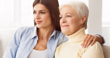 A younger woman is shown with her hand on the shoulder of an older woman as they sit together.