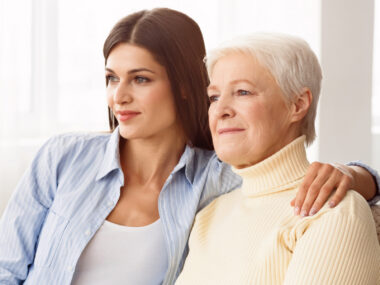 A younger woman is shown with her hand on the shoulder of an older woman as they sit together.