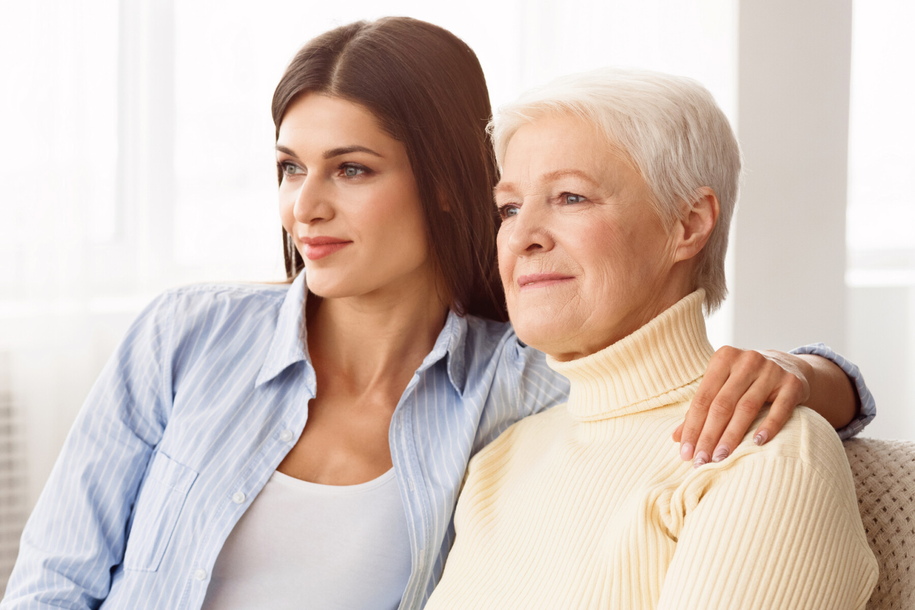 A younger woman is shown with her hand on the shoulder of an older woman as they sit together.