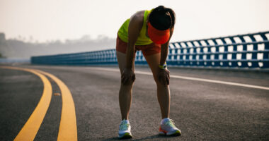 A photograph shows a woman bent over taking a breath while on a run.