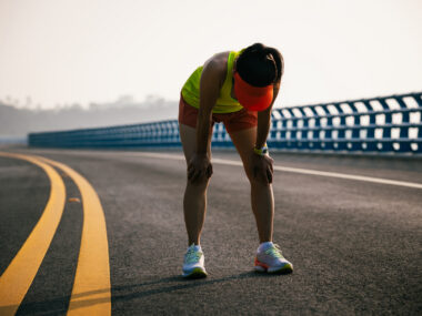 A photograph shows a woman bent over taking a breath while on a run.