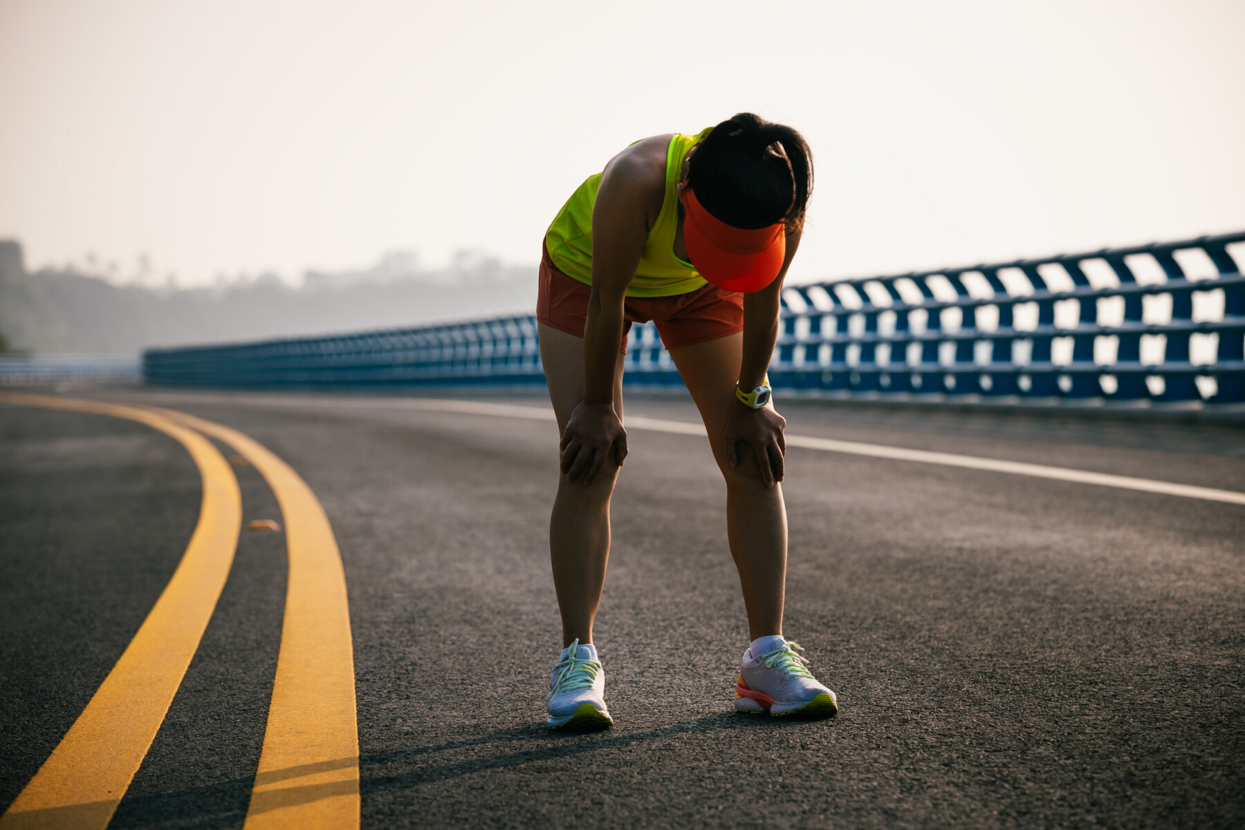 A photograph shows a woman bent over taking a breath while on a run.