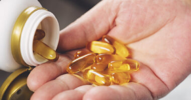 A hand holds gel capsules being dispensed from a pill bottle.