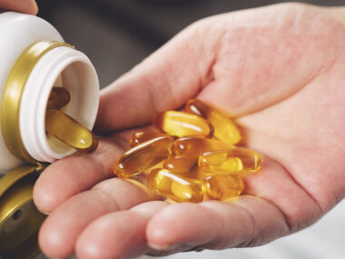 A hand holds gel capsules being dispensed from a pill bottle.